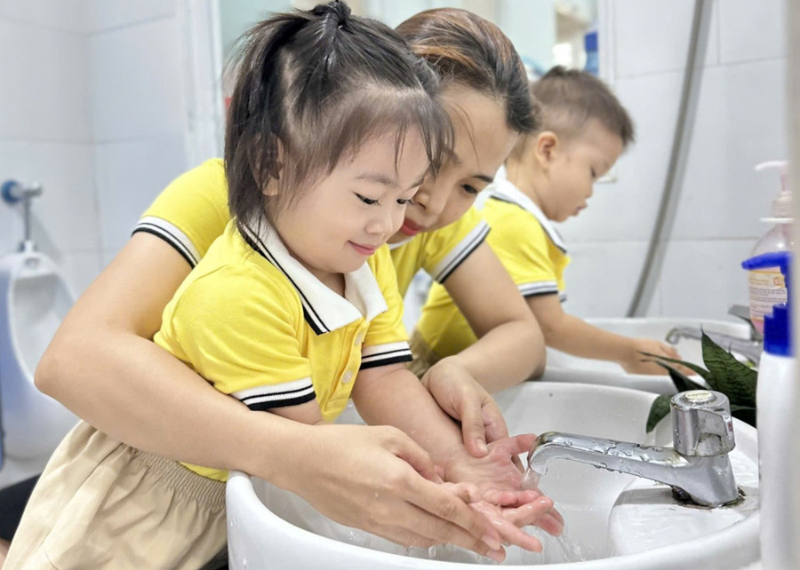 Bé ngoan ngoãn để cô giáo rửa tay
